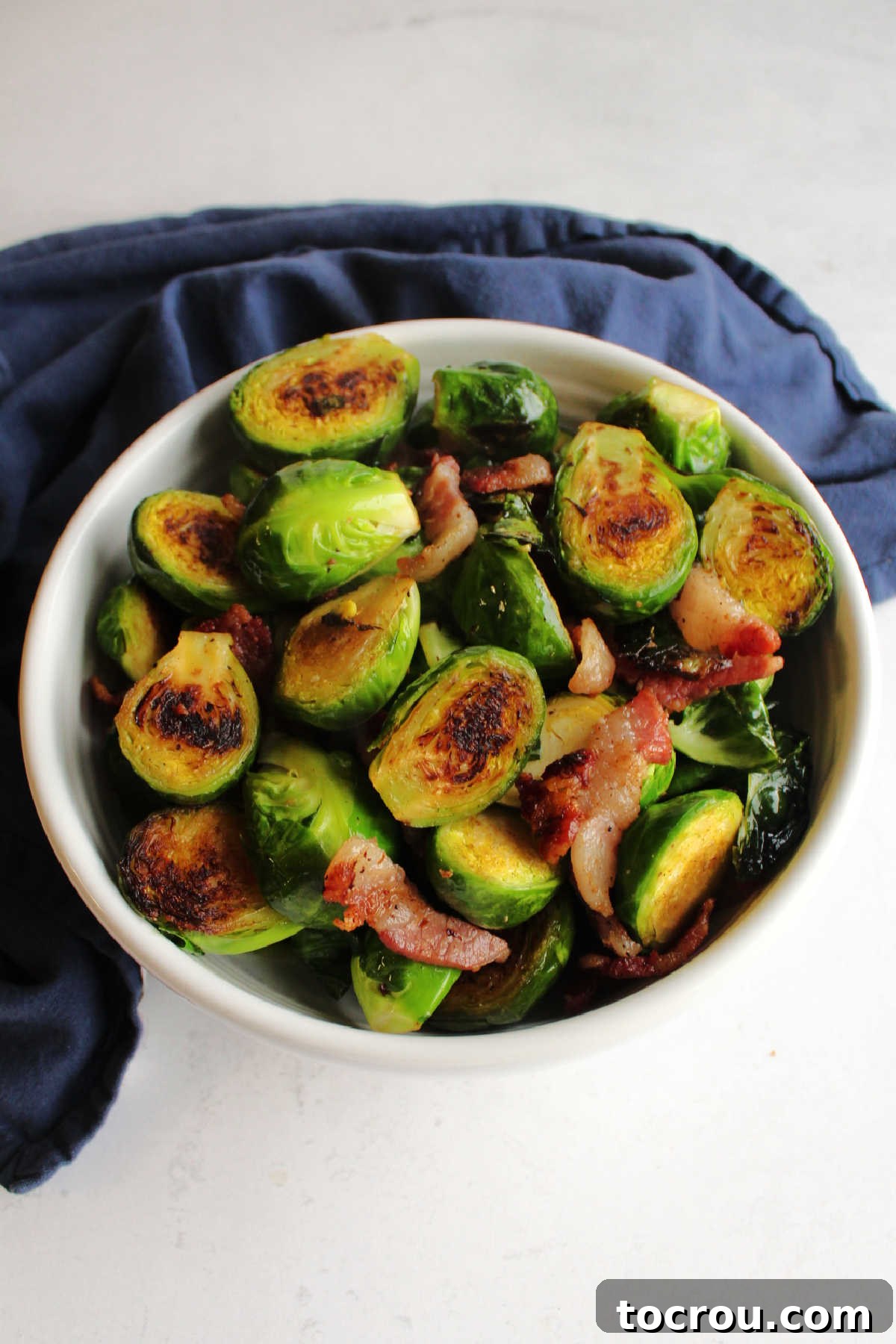 Serving bowl of golden brown Brussels sprouts and bacon, perfectly roasted and ready to eat.