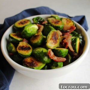 Serving bowl filled with golden brown Brussels sprouts halves and bits of bacon.