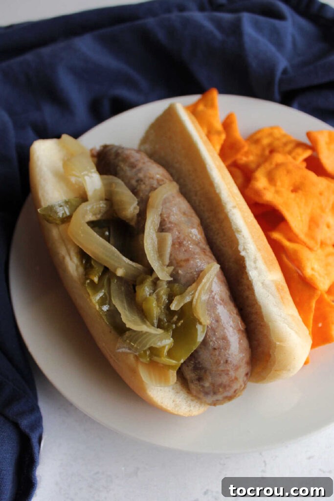 A plated slow cooker brat with caramelized onions and peppers, accompanied by a side of cheesy potato chips.