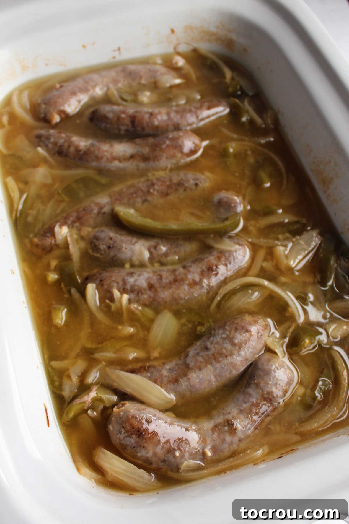 A slow cooker filled with perfectly cooked bratwursts, tender onions, and peppers, swimming in a rich beer broth, ready to be served.