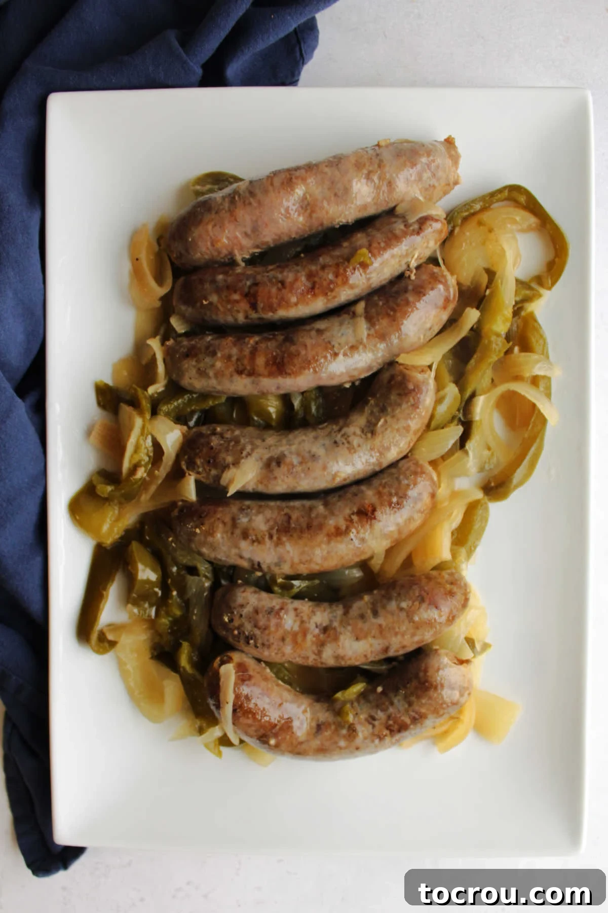 A serving platter brimming with cooked bratwursts, soft onions, and bell peppers, ready to be scooped onto buns.