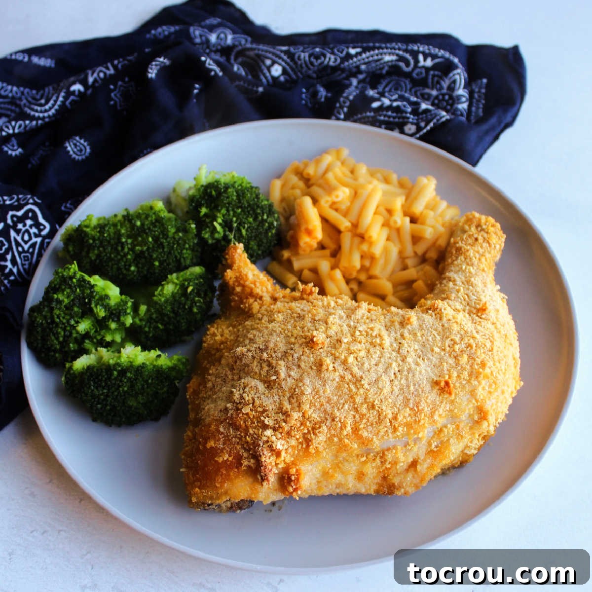 Dinner plate with cornflake crumb coated chicken leg quarter, mac and cheese and broccoli ready to eat.