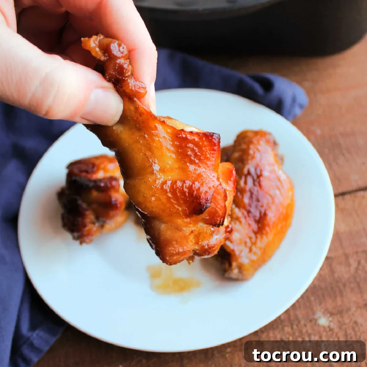 Sticky Caramelized Chicken Wings 2 Hand holding golden brown chicken wing with sticky sauce on it.