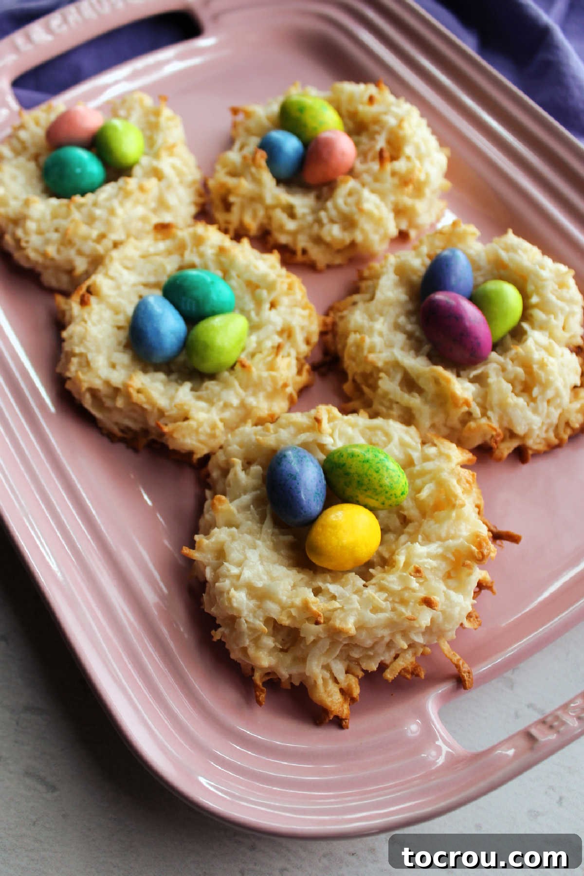 A pink ceramic platter showcasing five beautifully arranged coconut nests, each overflowing with an assortment of colorful candy eggs, ready for display.