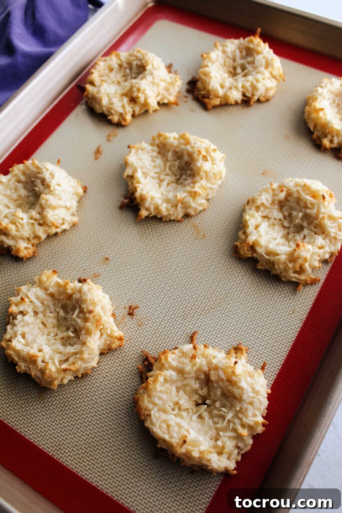 A baking tray filled with freshly baked coconut macaroon nests, displaying their golden-brown edges and inviting texture, straight out of the oven.