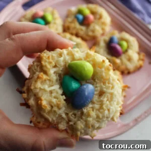 Hand holding coconut macaroon nest filled with candy eggs.