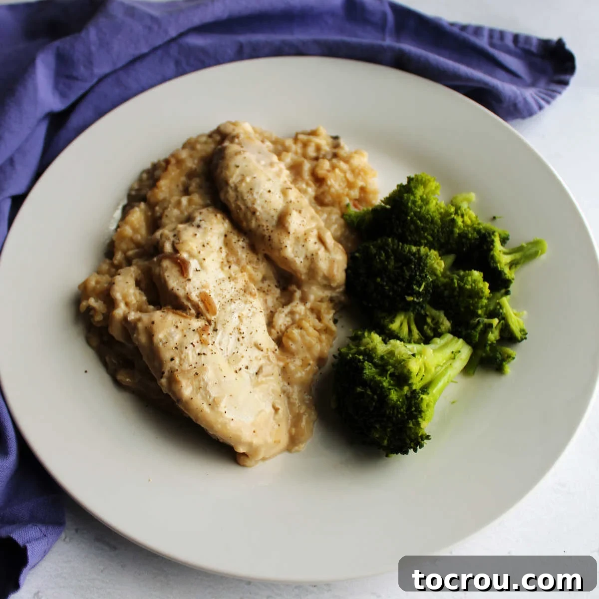 A dinner plate featuring creamy slow cooker chicken and rice, garnished with fresh parsley and a side of vibrant green broccoli, ready to enjoy.