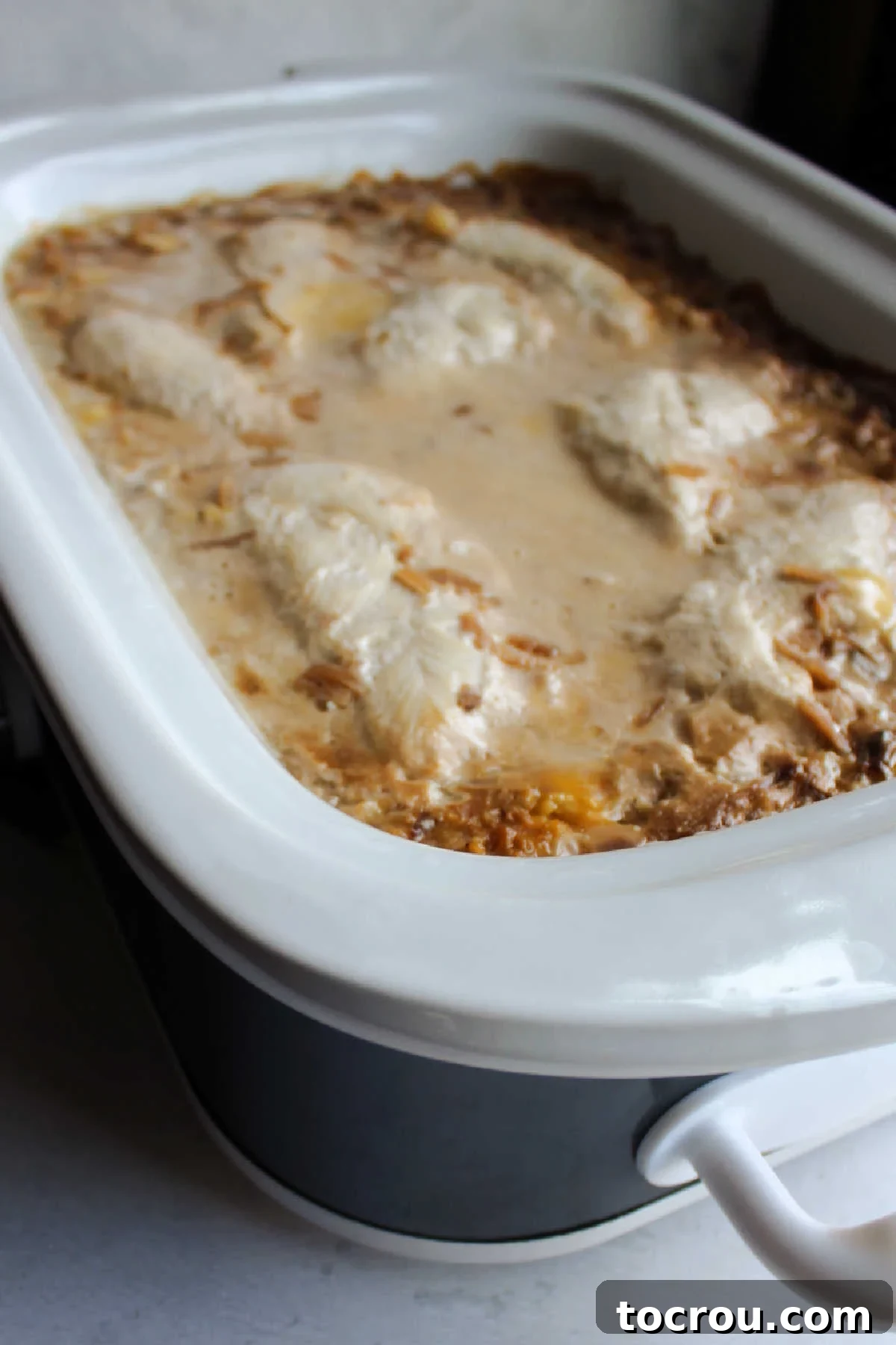 Cooked chicken and creamy rice in a slow cooker, steam gently rising, indicating it's hot and ready to be served.