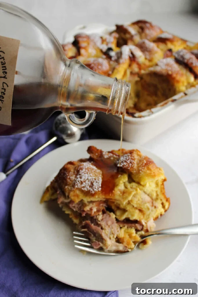 Maple syrup being poured generously over a warm slice of Monte Cristo brunch bake, capturing the sweet and savory essence of the dish.