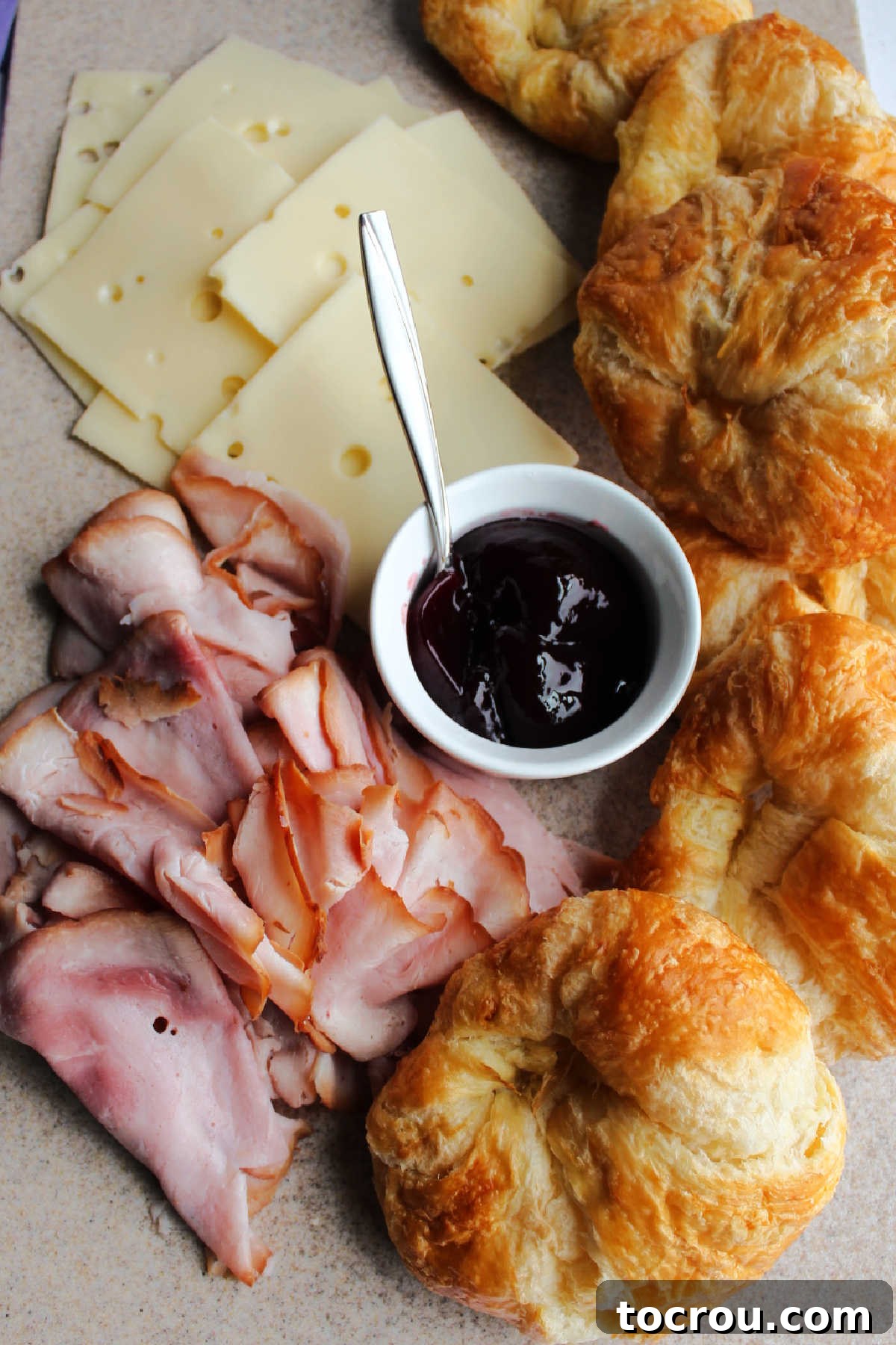 Ingredients laid out: croissants, sliced ham, Swiss cheese, and raspberry preserves, meticulously arranged for casserole assembly.