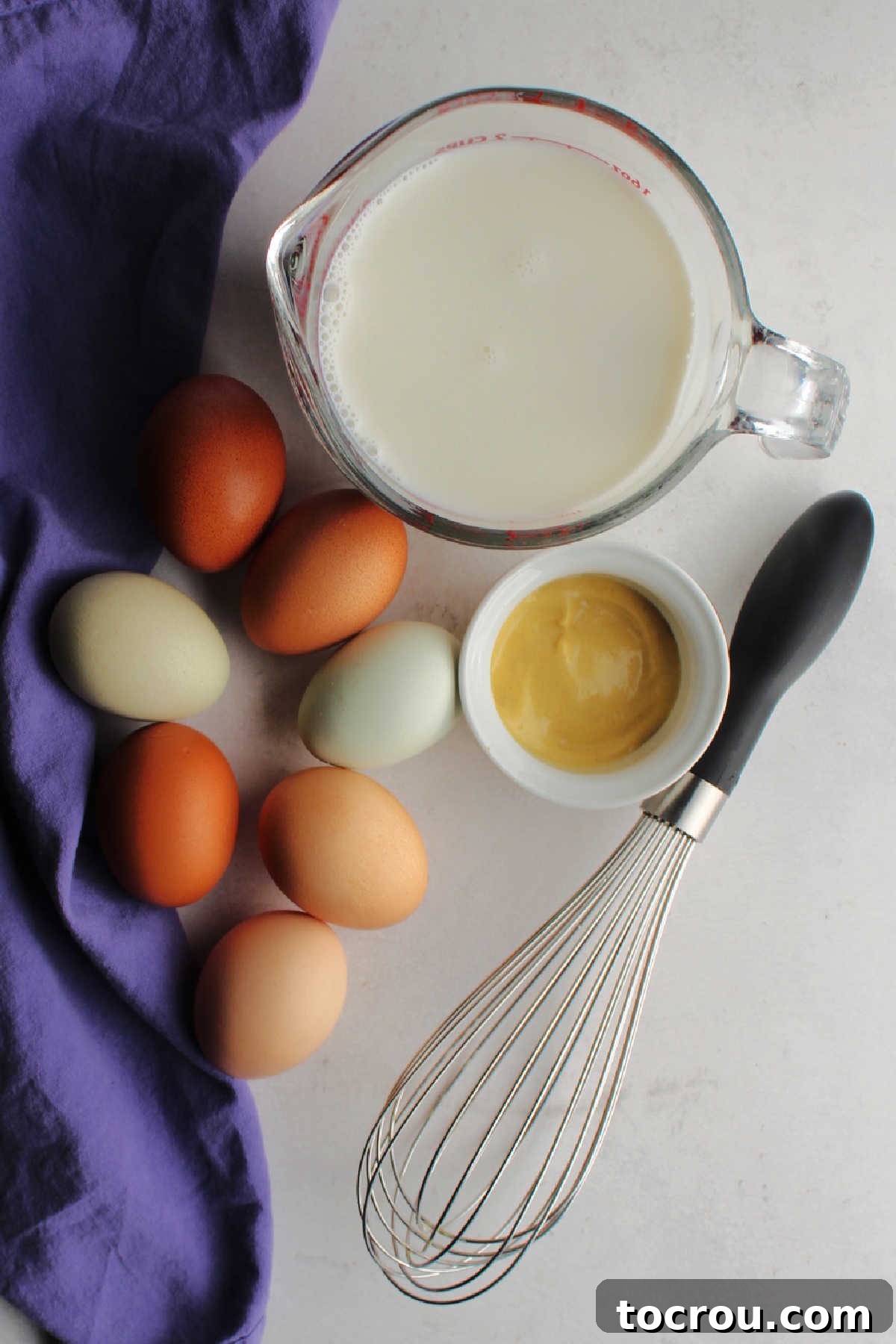 A bowl containing eggs, half and half, and a dollop of Dijon mustard, prepared for whisking into the rich and flavorful custard.