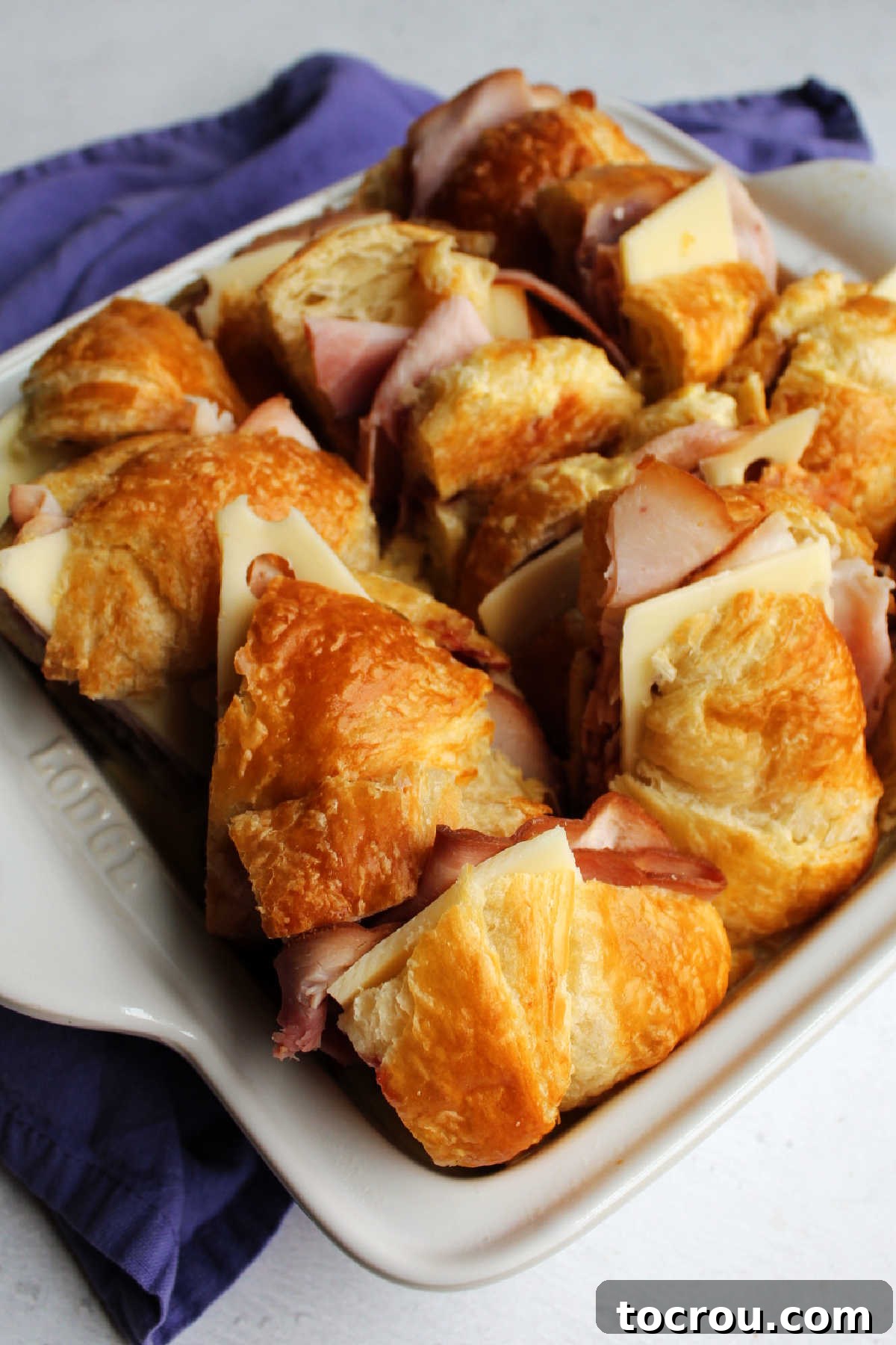 Half-cut ham, cheese, and raspberry sandwiches meticulously arranged in a greased baking dish, awaiting the flavorful custard pour.