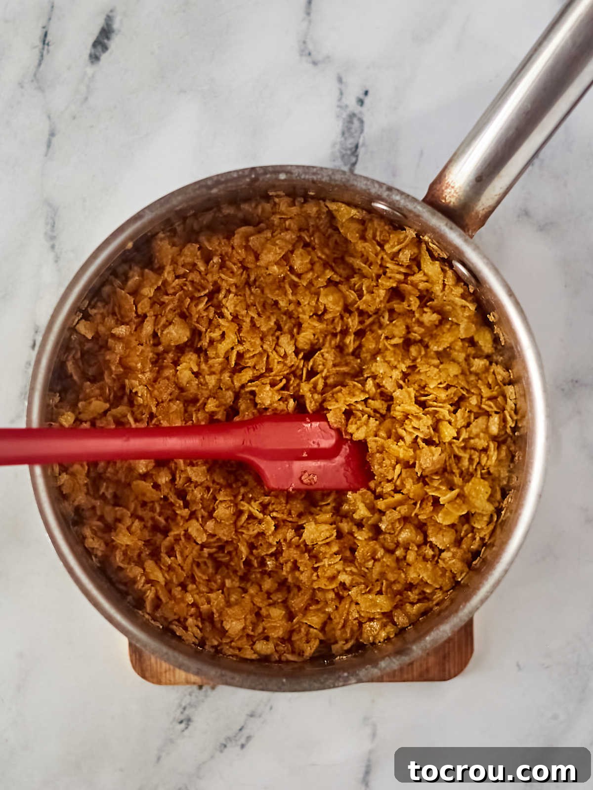 Pan of crushed cornflake bits coated in butter and sugar mixture to make crunchy bits of unfried ice cream bars.