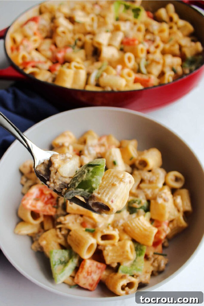 Creamy Chorizo Pasta on a Fork A fork lifts a medley of pasta, cooked chorizo chunks, and vibrant peppers, all generously coated in a rich, creamy cheese sauce, poised for a delightful bite.