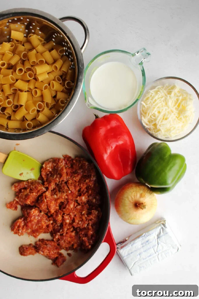 Creamy Chorizo Pasta Ingredients A selection of fresh ingredients including chorizo, bell peppers, onion, pasta, milk, cream cheese, and shredded Monterey Jack cheese, laid out on a kitchen counter, ready for cooking.