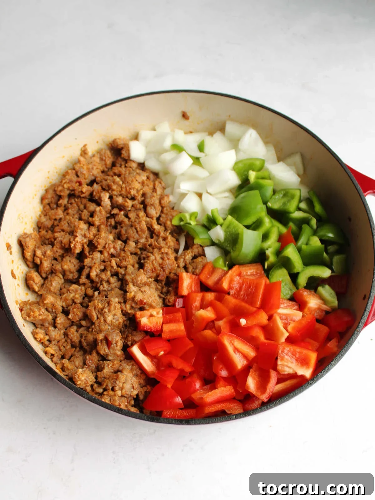 Browning Chorizo and Vegetables Fresh chorizo is browned in a pan alongside chopped red bell pepper, green bell pepper, and onion, preparing for further cooking and integration into the dish.