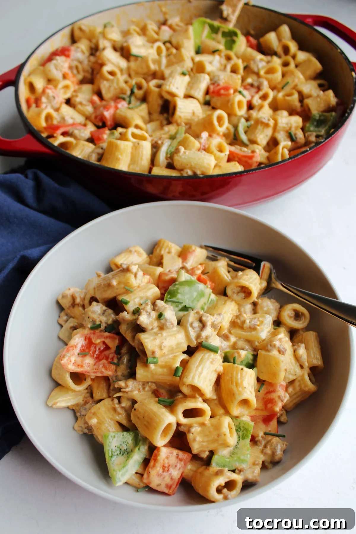 Ready to Serve Creamy Chorizo Pasta A bowl filled with creamy chorizo pasta, showcasing its rich texture and colorful ingredients, is placed in front of a large pan containing the remaining pasta, highlighting a freshly prepared and plentiful meal.