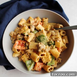 Serving of creamy chorizo pasta with chunks of green and red pepper an onions in bowl with a fork ready to eat.