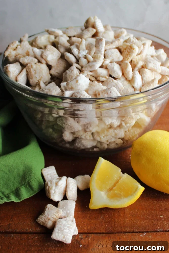 A bowl of powdered sugar-coated lemon puppy chow, garnished with a fresh lemon wedge, showcasing its delicious finish.
