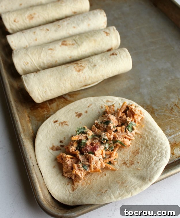 Rolling Taquitos Close-up of creamy cheesy chicken mixture spread onto a flour tortilla, prepared for rolling into a taquito before baking.