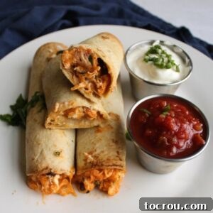 Close-up of a creamy chicken taquito, cut open to reveal the rich filling, with dipping sauces in the background.