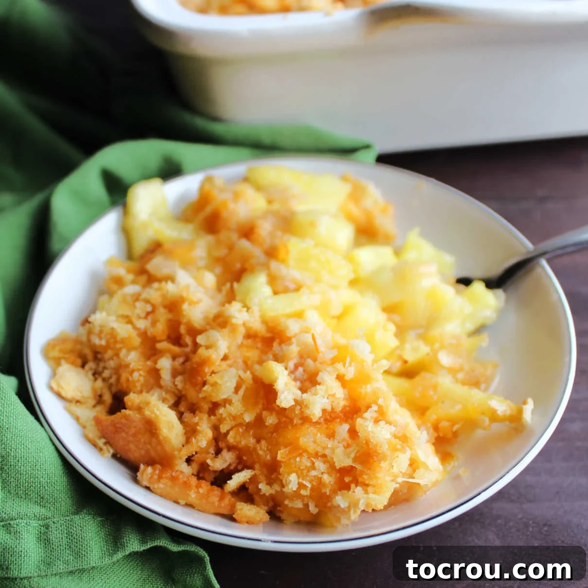 Small dish filled with pineapple casserole topped with buttery cracker crumbs and cheese.