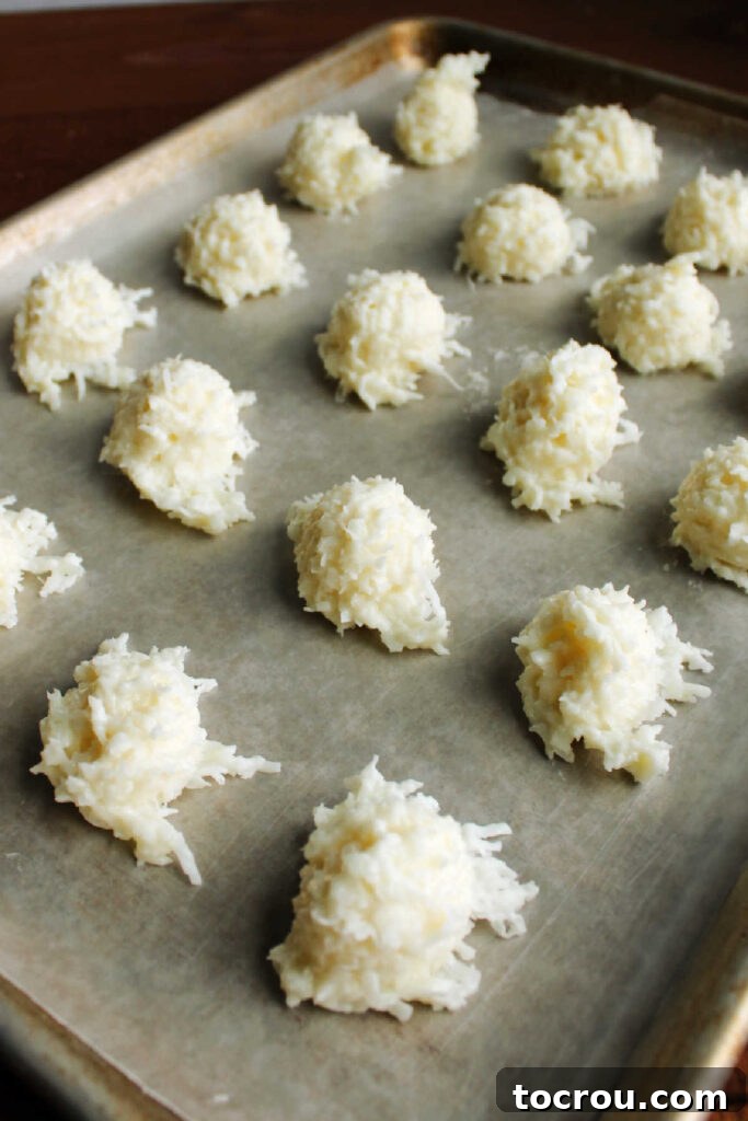 Portioned scoops of the creamy coconut mixture, with visible shredded coconut texture, laid out on parchment paper.