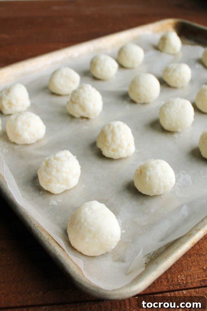 Smooth, perfectly rounded frozen coconut truffle centers arranged on a sheet pan, ready for dipping.
