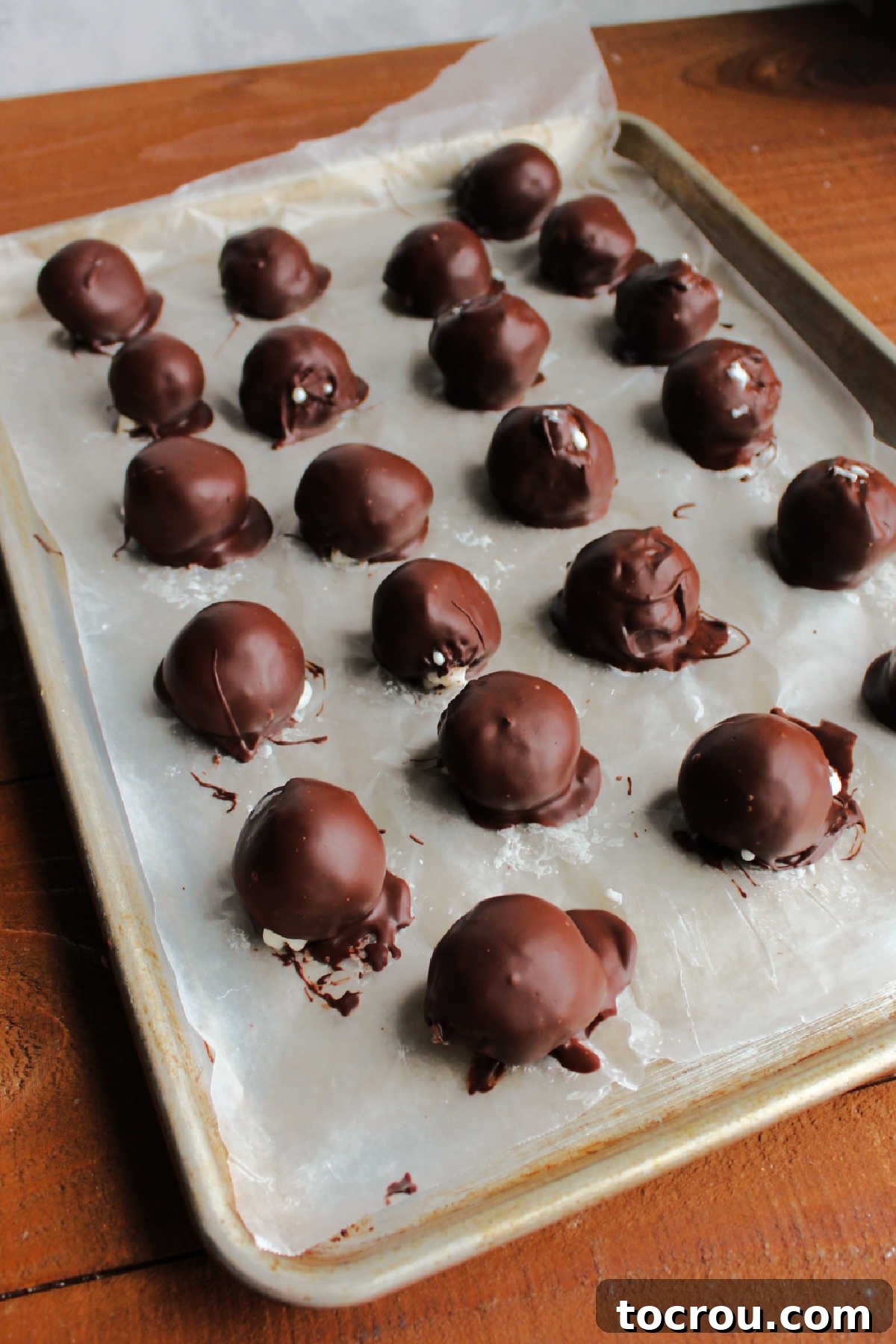 Freshly chocolate-dipped coconut truffles arranged on wax paper, allowing the chocolate coating to set and harden.