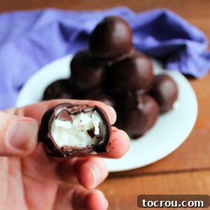 Hand holding a homemade Mounds-style candy, revealing the creamy coconut center and chocolate shell.