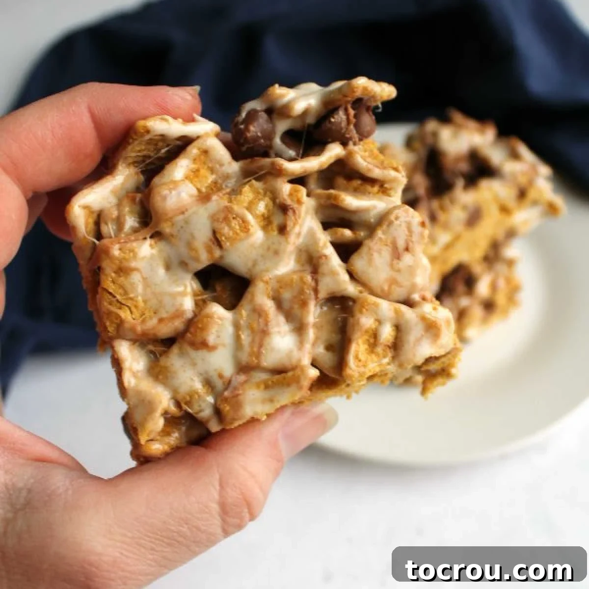 Delicious No-Bake S'mores Bar Hand holding a gooey, marshmallowy s'mores bar with golden graham cereal and melty chocolate chips, ready to eat.