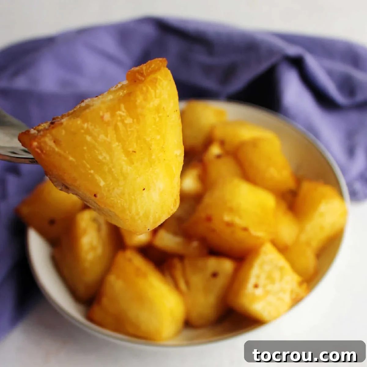 Chunk of air fried pineapple coated in butter and brown sugar on fork, ready to eat.