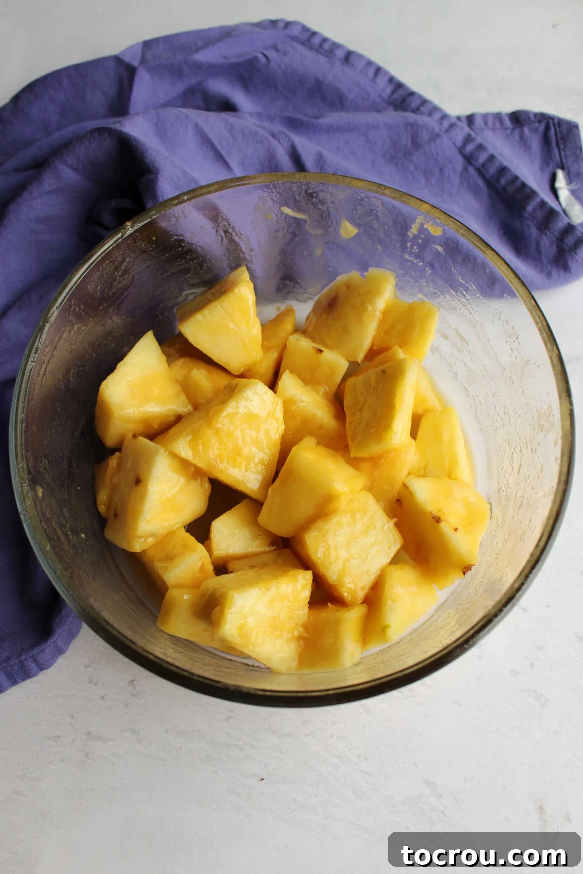 Bowl of pineapple chunks tossed in melted butter and brown sugar, ready to cook.