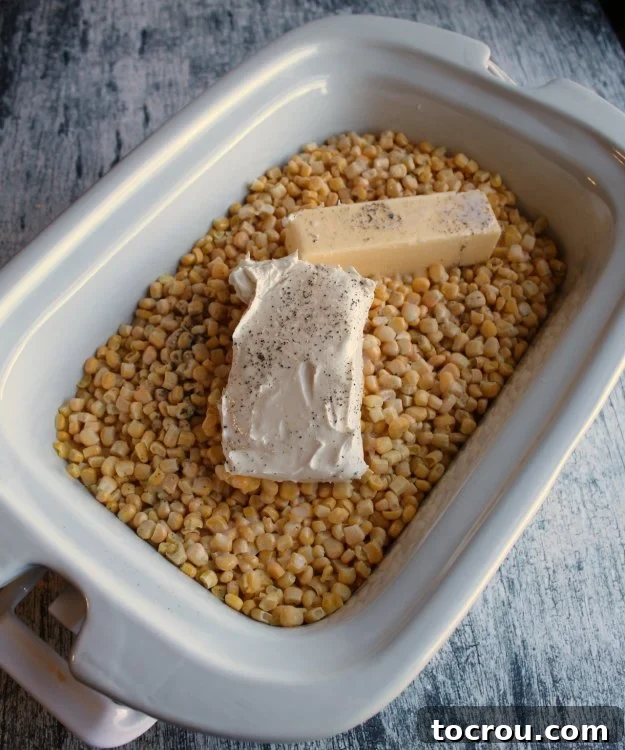 Simple Ingredients for Crockpot Creamed Corn Fresh corn kernels, cubes of butter, and a block of cream cheese nestled in a slow cooker, poised to transform into creamy deliciousness.