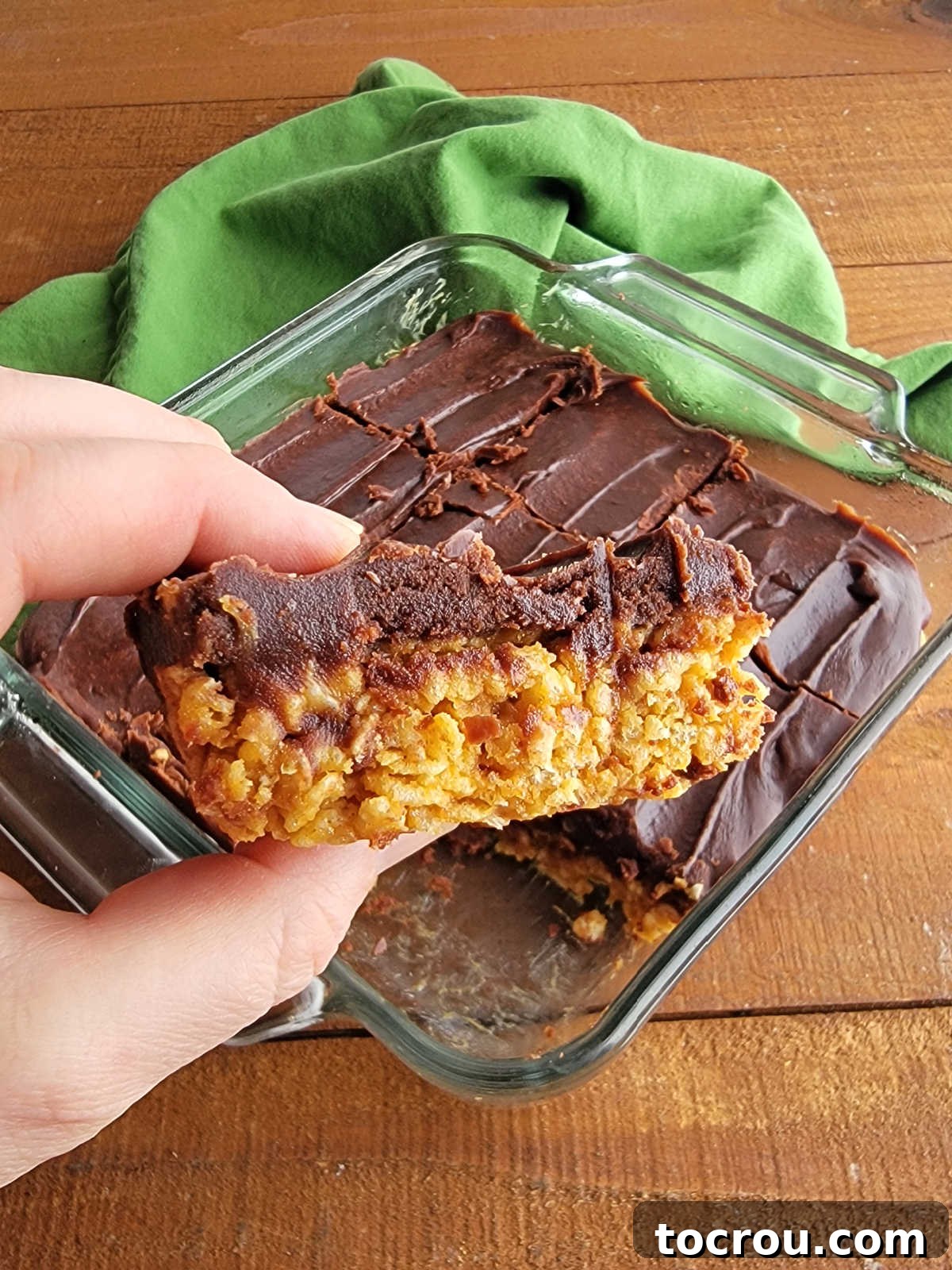 Hand holding a chocolate-frosted maple peanut butter rice krispie treat, ready to be enjoyed.