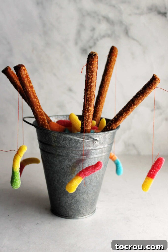 Camping Party Snacks - Fishing Poles Small metal bucket holding pretzel rods designed to look like fishing poles, complete with gummy worms dangling from the ends.