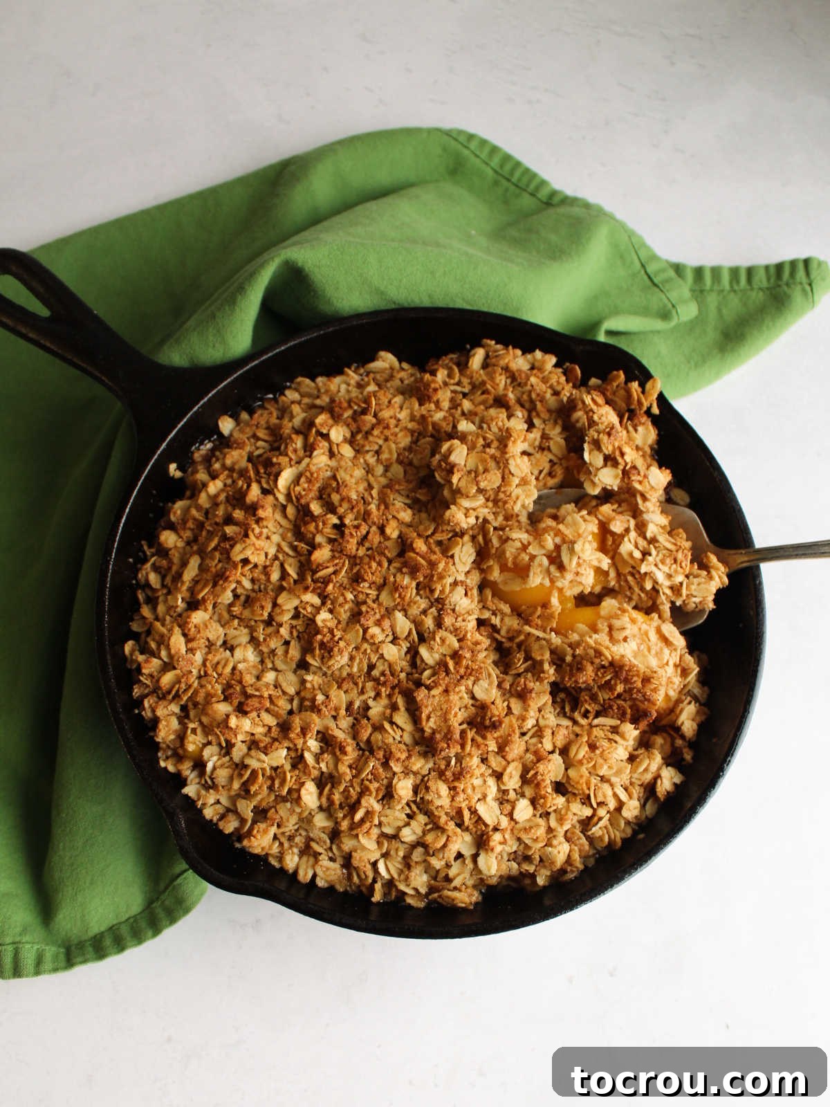 Cast iron pan filled with peach crisp, fresh from the oven, with a perfectly golden and bubbly topping.