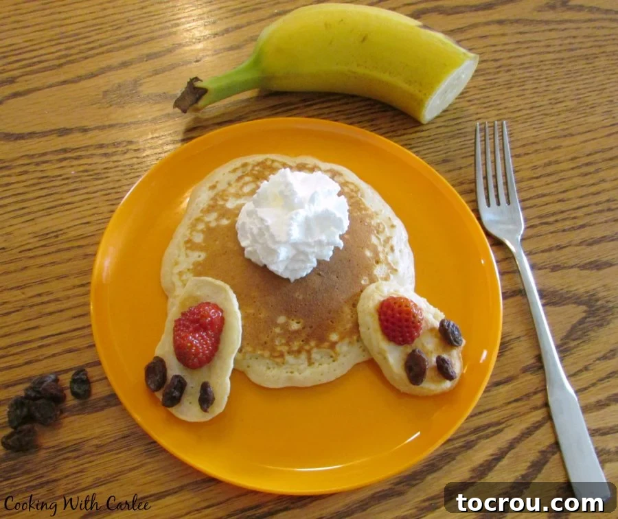 A child's orange plate holds a cheerful bunny butt pancake, thoughtfully garnished with banana slices and extra raisins, ready for a fun Easter meal.