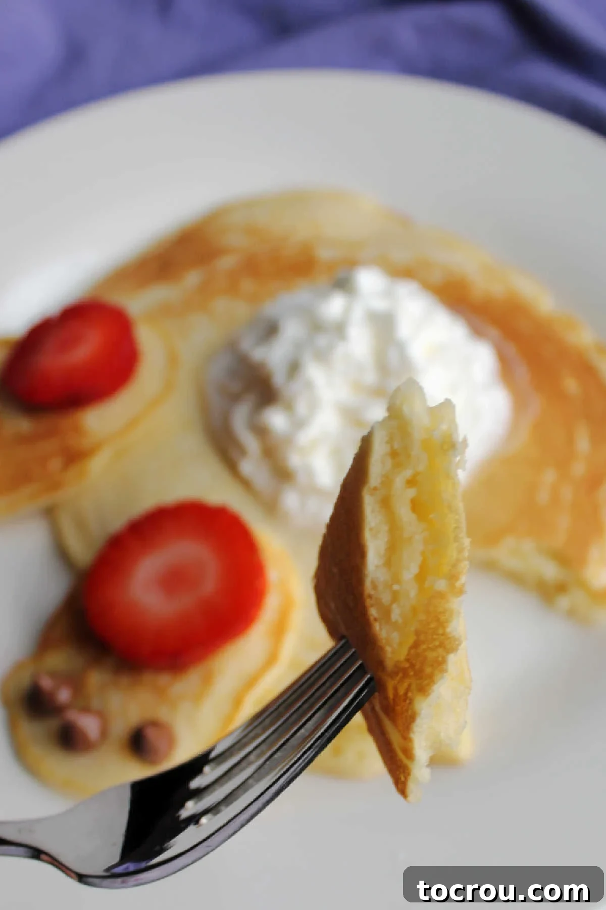 A close-up shot captures a fork lifting a fluffy bite of pancake, with a decorated bunny butt pancake softly blurred in the background, highlighting the irresistible texture.