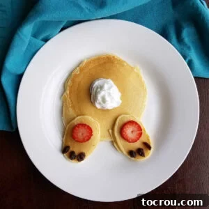 Pancakes decorated to look like bunny butt with whipped cream tail and strawberry and raisin feet.