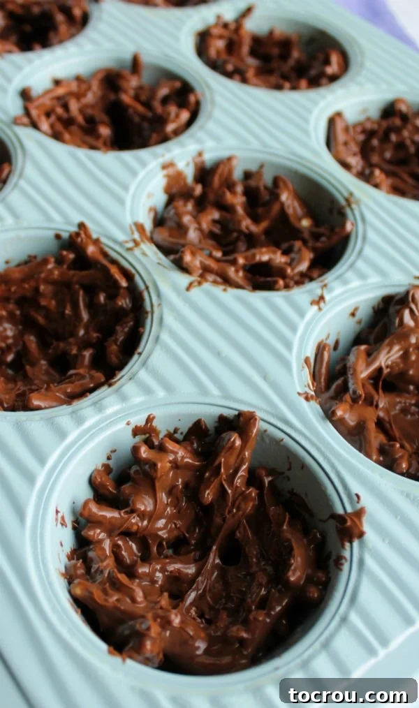 Chocolate and chow mein mixture in cupcake tin being shaped like nests.