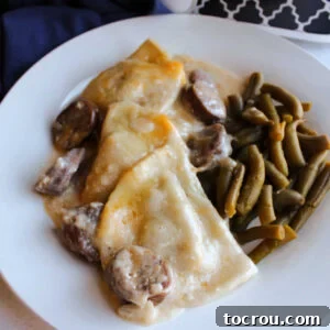 A close-up view of a comforting casserole featuring cheesy pierogies and savory chunks of kielbasa in a rich sour cream sauce, served alongside fresh green beans.