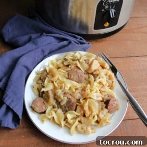 A generous serving of crockpot haluski, featuring tender cabbage, egg noodles, and savory kielbasa, with the slow cooker visible in the background.