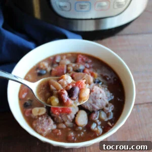 A spoon brimming with delicious bean soup, featuring tomatoes and kielbasa, held over a bowl of the soup next to an Instant Pot.