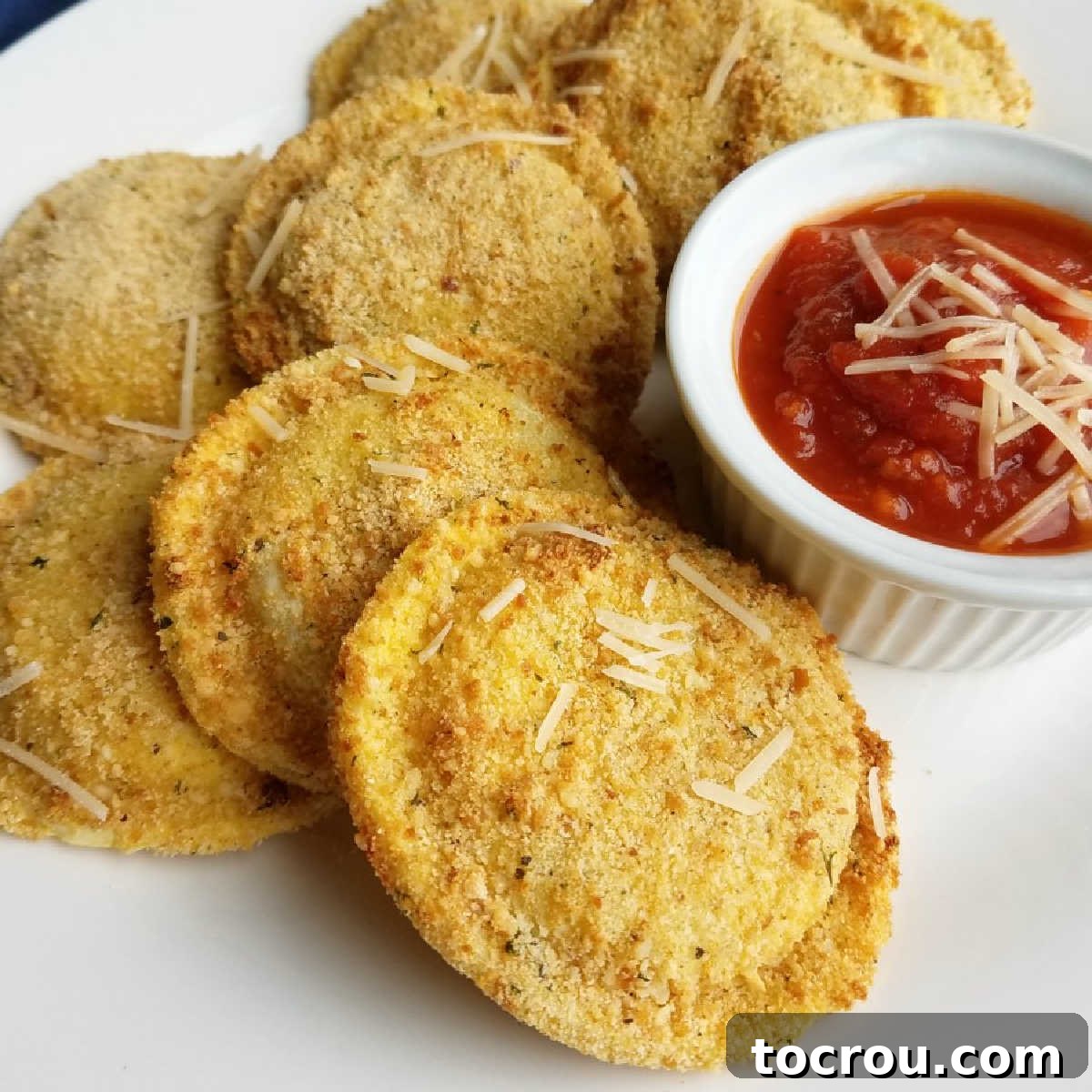 Close up of golden crispy air fryer toasted ravioli served with a ramekin of rich marinara dipping sauce.