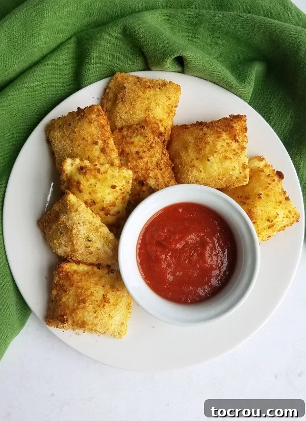 Square-shaped toasted ravioli arranged neatly around a small bowl of marinara sauce, garnished with fresh herbs.