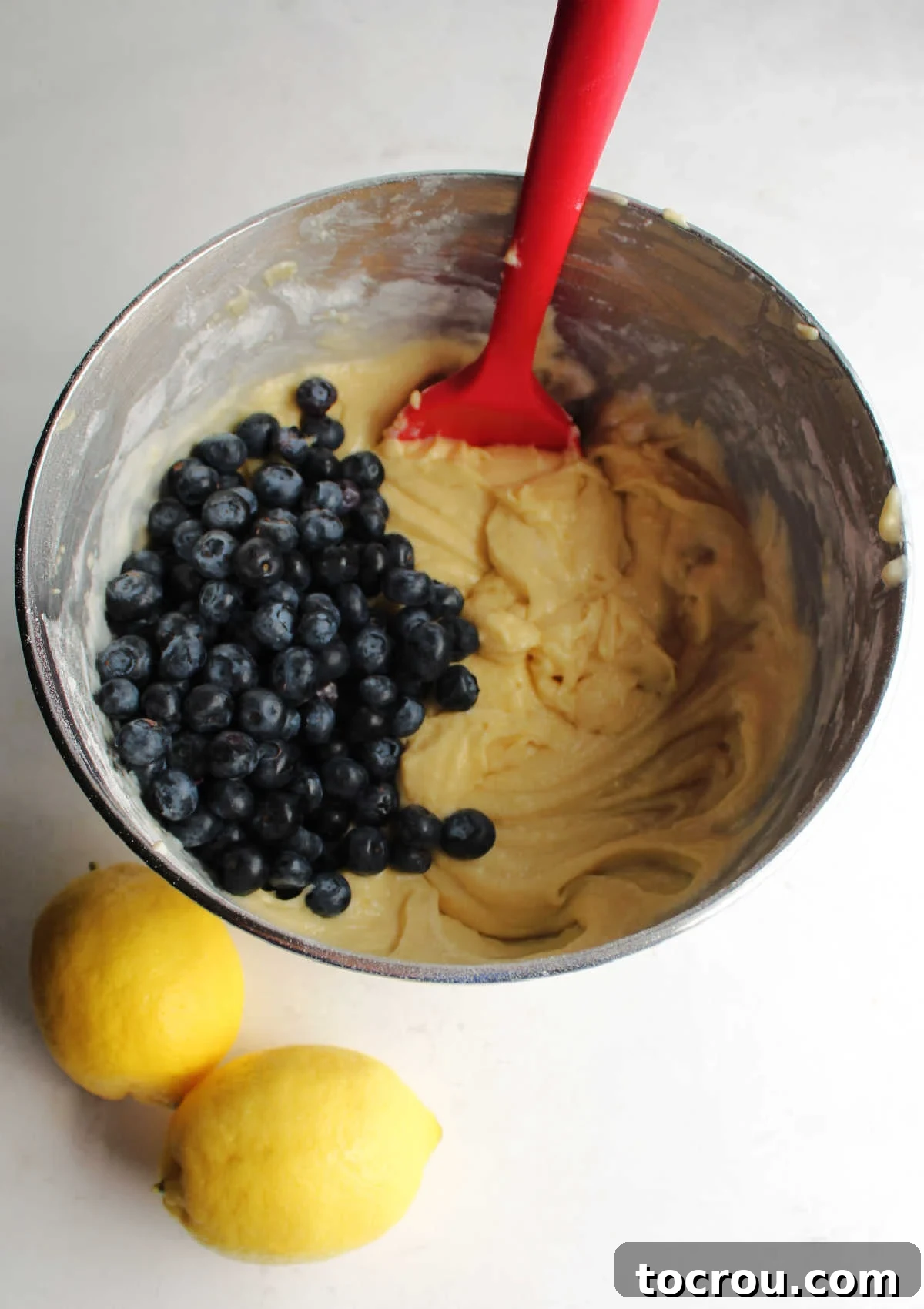 Lemon Blueberry Bliss Bundt 5 A mixing bowl filled with creamy lemon cake batter, with fresh blueberries waiting to be gently stirred in.