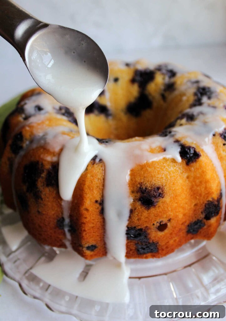 Lemon Blueberry Bliss Bundt 9 Pouring a vibrant lemon and powdered sugar glaze over a blueberry Bundt cake, creating a beautiful sweet topping.