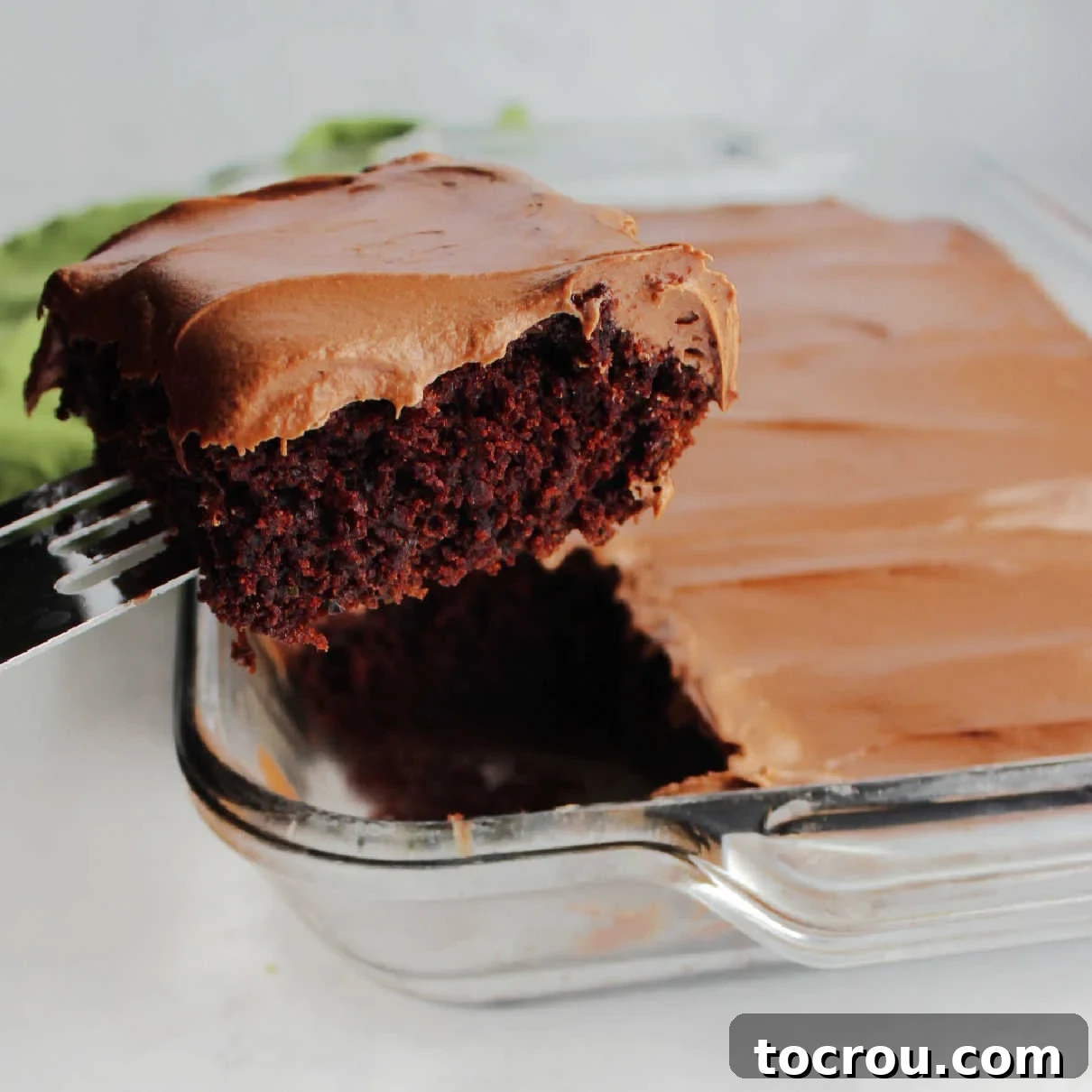 Lifting piece of chocolate zucchini cake out of pan, showcasing its moist texture.