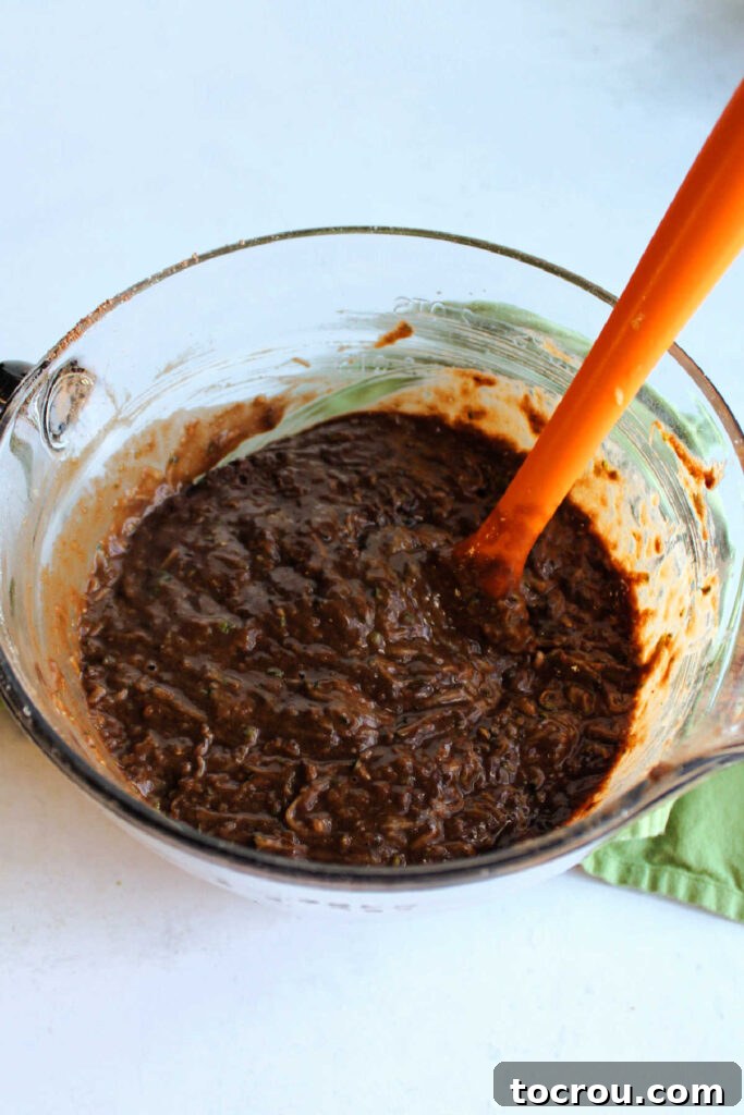Bowl of chocolate cake batter with shredded zucchini inside, transforming into a moist mixture.
